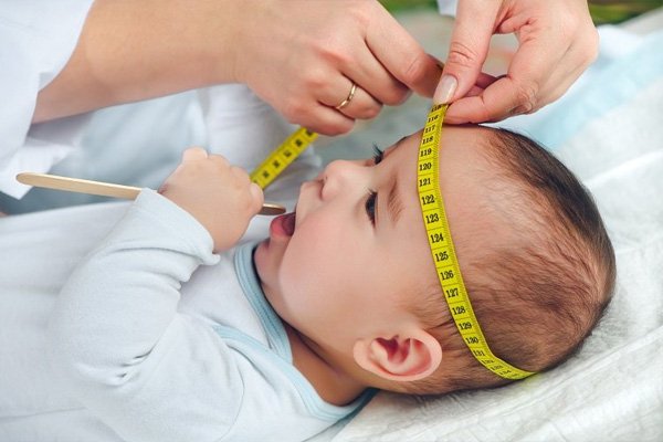 Measuring tape checking a young child's head circumference at a growth visit